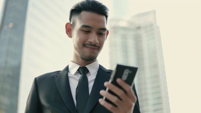 Happy handsome young businessman using a smartphone texting checking email messages online and uses social networks while standing on the street urban.
