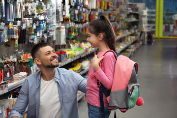 Little girl with father choosing school stationery in supermarket
