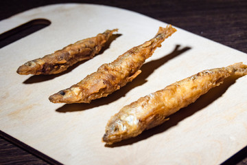 Three little fried fish on a wooden cutting board.