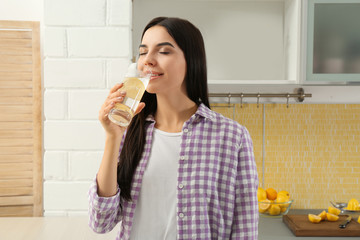 Beautiful young woman drinking lemon water in kitchen