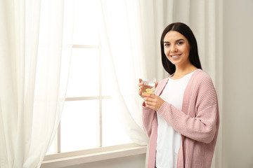 Beautiful young woman with tasty lemon water near window