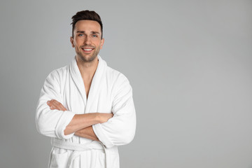 Happy young man in bathrobe on light grey background. Space for text