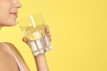 Young woman drinking lemon water on yellow background, closeup. Space for text