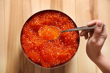 Woman holding spoon with fresh red caviar at wooden table, top view
