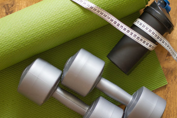 sports equipment for fitness. Green yoga Mat, with black water bottle and grey dumbbells. Space for text. For sports at home. the concept of sport, beauty and health.