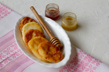 a white plate of cheesecakes and two jars of honey on a white table. space for text. the concept of the menu. five cheesecakes. delicious and beautiful Breakfast. the layout of the food. food for a ch