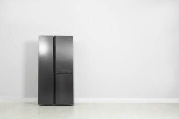 Modern refrigerator near light grey wall, space for text