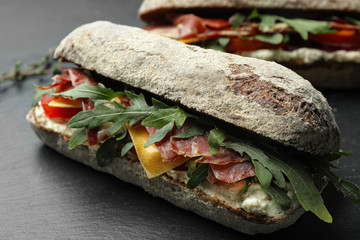 Delicious sandwich with fresh vegetables and prosciutto on grey table, closeup