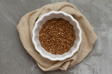 Buckwheat in A white dish on a wooden gray table. The view from the top. Space for text. delicious and healthy food and nutrition. vitamins for humans. cereals and grains.