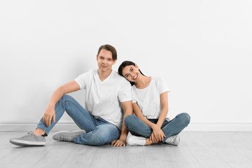 Fototapeta na wymiar Young couple in stylish jeans sitting near white wall