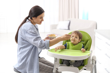 Young nanny feeding cute little baby at home