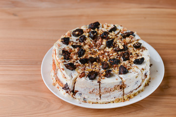 Vanilla sponge cake biscuit with prune, walnuts and frosting served on a white plate, on light wooden background table