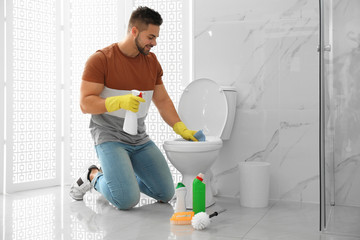 Young man cleaning toilet bowl in bathroom