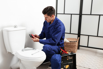 Professional plumber working with toilet bowl in bathroom