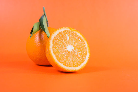 closeup of full and half cut fresh juicy orange on orange color backdrop citrus fruits