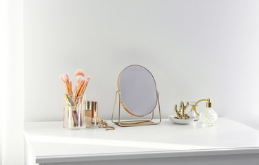 Small mirror and makeup products on white dressing table indoors