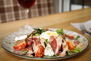 Delicious prosciutto salad with vegetables served on wooden table indoors