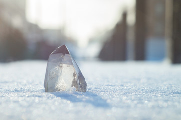 Snow-white crystal of pure transparent quartz on snow. Chalcedony contrast on background of blurred city lines - obrazy, fototapety, plakaty