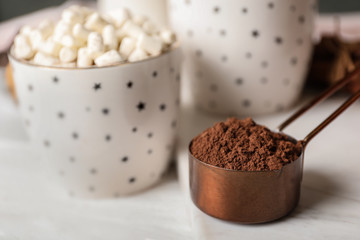 Cocoa powder in scoop and hot drink on white wooden table