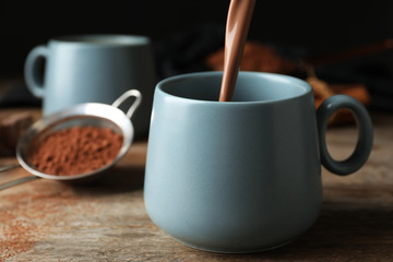 Pouring hot cocoa drink into cup on wooden table