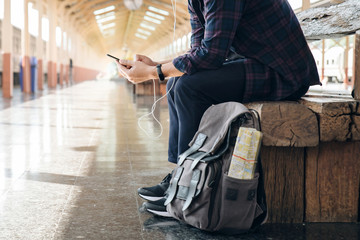 Young man traveler sitting with using mobile phone choose where to travel and bag waiting for train...