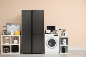 Modern refrigerator and other household appliances near beige wall indoors