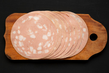 Top view, sliced Mortadella Bologna Meat on a rustic wooden board over black surface, top view. Flat lay, from above, overhead. Close-up. © Liudmyla