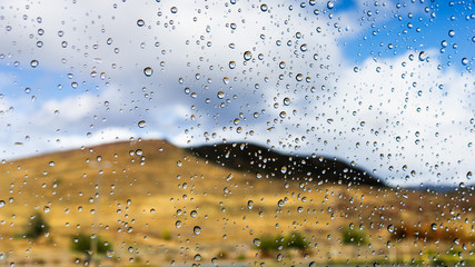 Drops of rain on the window on a rainy winter day in Los Angeles County, California; blurred hills covered by dry grass visible in the background; shallow depth of field;