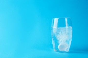 Glass of water with effervescent tablet on light blue background, space for text