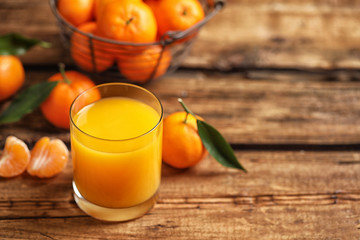 Glass of fresh tangerine juice and fruits on wooden table. Space for text