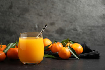 Glass of fresh tangerine juice and fruits on black table. Space for text