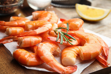 Delicious cooked shrimps with rosemary on wooden board, closeup