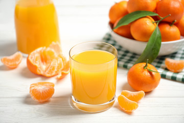 Glass of fresh tangerine juice and fruits on white wooden table
