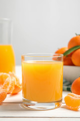 Glass of fresh tangerine juice and fruits on white wooden table