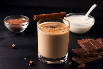 lassi chocolate drink on a black background next to the ingredients yogurt, cocoa and chocolate