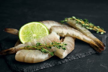 Fresh raw shrimps with lime and thyme on black table, closeup