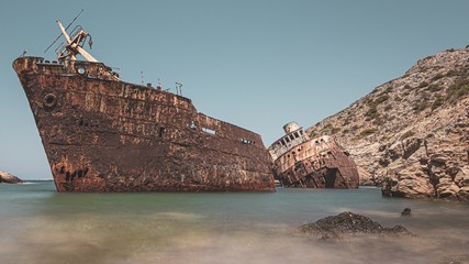 Abandoned rusty ship in the sea near huge rock formations