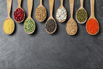 Flat lay composition with different types of legumes and cereals on dark grey table, space for text. Organic grains
