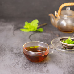 Cup of hot mint tea  and fresh mint leaves on concrete background. Relax beverage concept