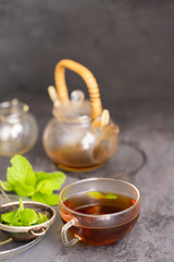 Cup of hot mint tea  and fresh mint leaves on concrete background. Relax beverage concept
