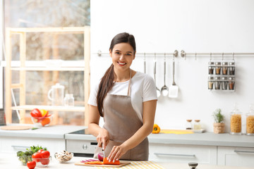 Young woman cutting vegetables for soup at table in kitchen