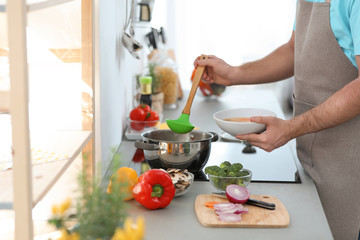 Obraz na płótnie Canvas Young man pouring delicious soup into bowl at home, closeup