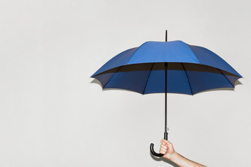 A man holds a blue umbrella in his hand against a gray wall. Open space. Concept autumn, color of the year 2020, business, protection - obrazy, fototapety, plakaty
