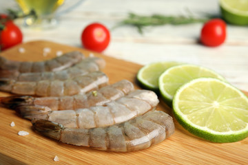 Fresh raw shrimps and lime on wooden board, closeup