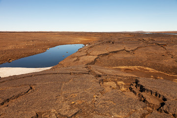 Fototapeta premium Small cold lake on a dry cracked earth on a calm deserted spring landscape of Iceland
