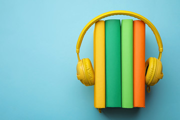 Books and modern headphones on light blue background, top view. Space for text
