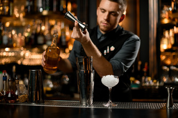 Bartender pours cognac from jigger to shaker