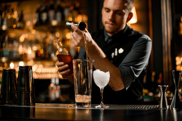 Bartender making alcohol cocktail with a steel jigger