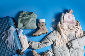 Suitcase with warm clothes on light blue background, flat lay. Winter vacation