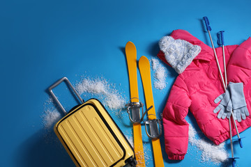 Suitcase with warm clothes and skis on light blue background, flat lay. Winter vacation